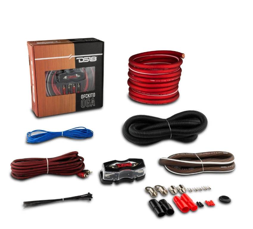 DS18 OFCKIT0 0-gauge OFC amplifier wiring kit complete contents flat lay showing retail box, 17-ft red OFC power cable with ring terminal, black loom tube, red, black twisted RCA cable, blue remote wire, ANL fuse holder, black speaker wire, zip ties, ring terminals, fork terminals, butt connectors, and rubber grommet