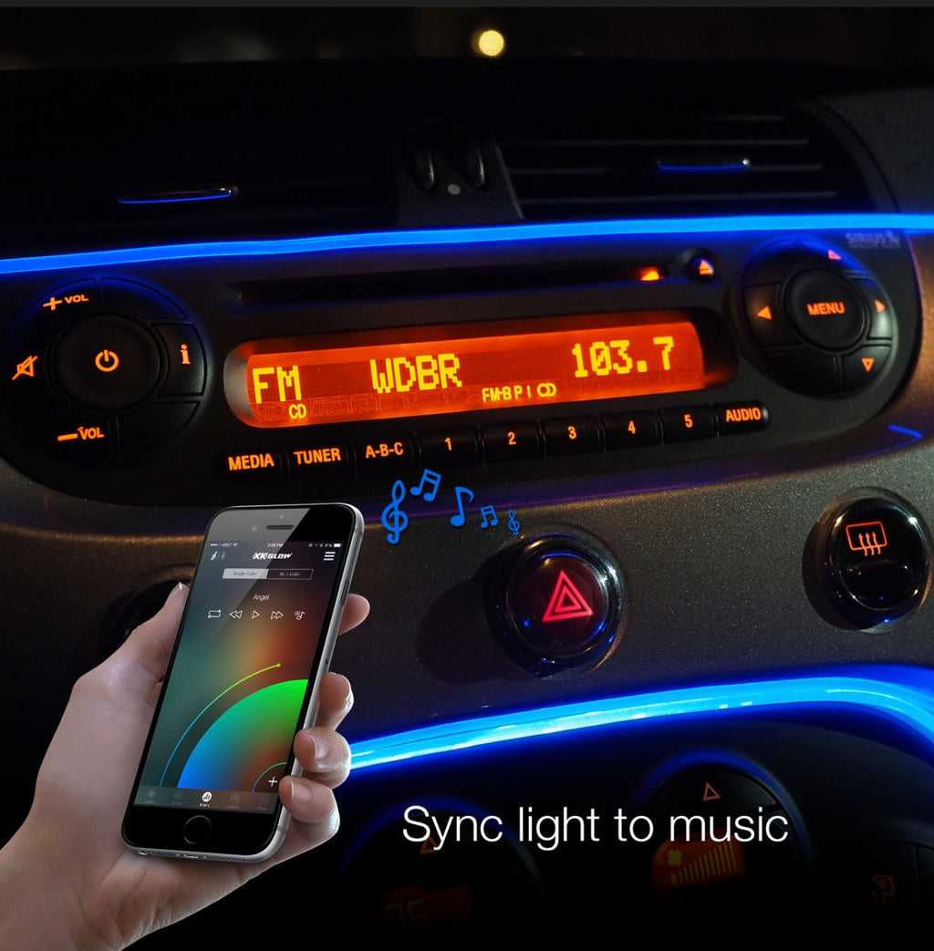 A hand holds a smartphone in front of a car dashboard, with blue LED ambient lighting synchronized to the phone's music display. The dashboard features illuminated controls, an orange radio screen, and the text 'Sync light to music' at the bottom.