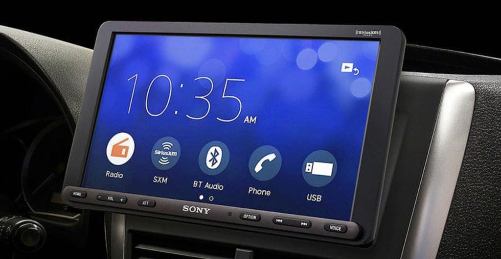 Sony XAV-AX8100 installed in vehicle dash showing home menu with 10:35 AM clock display and Radio, SiriusXM, BT Audio, Phone, and USB shortcut icons