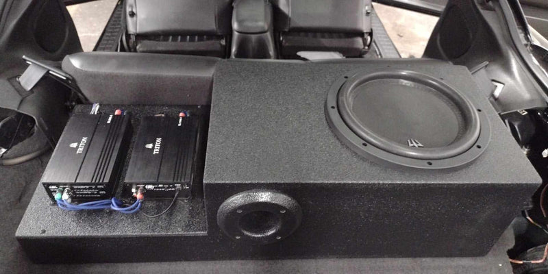 A black car subwoofer speaker system installed in a vehicle trunk, including a large subwoofer box and two power amplifiers
